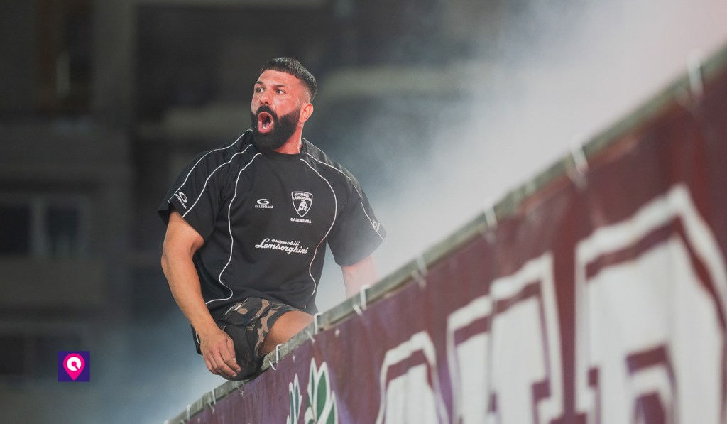 Lubrano, ultras della Reggina, urla seduto sulla balaustra della curva con uno striscione amaranto e fumo alle spalle
