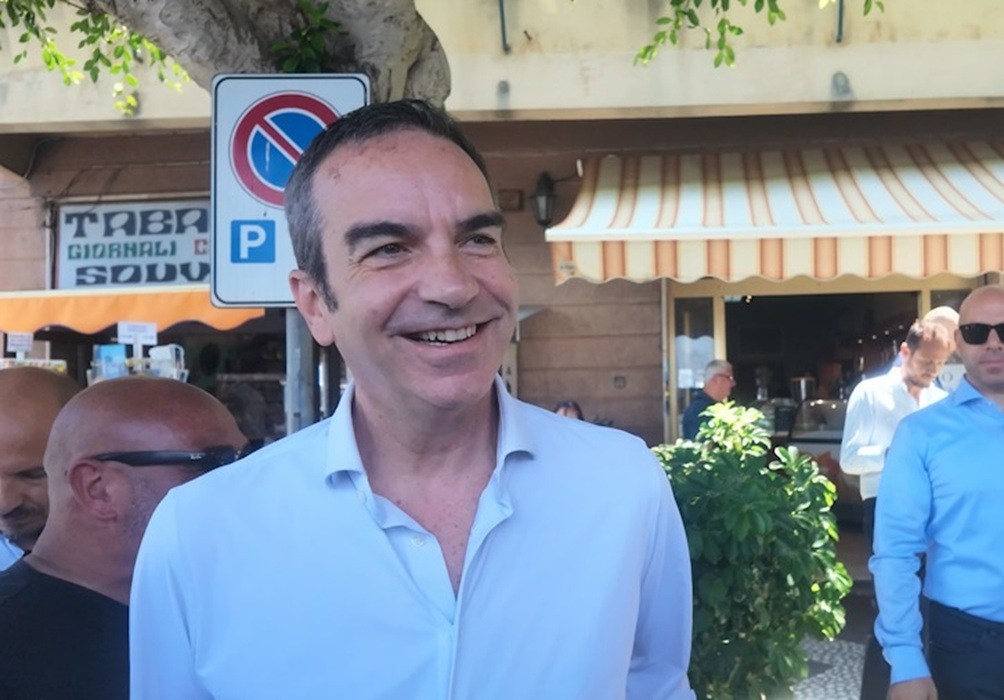 Roberto Occhiuto, presidente della Regione, sorride in strada davanti a un bar tabacchi per la presentazione di UberX