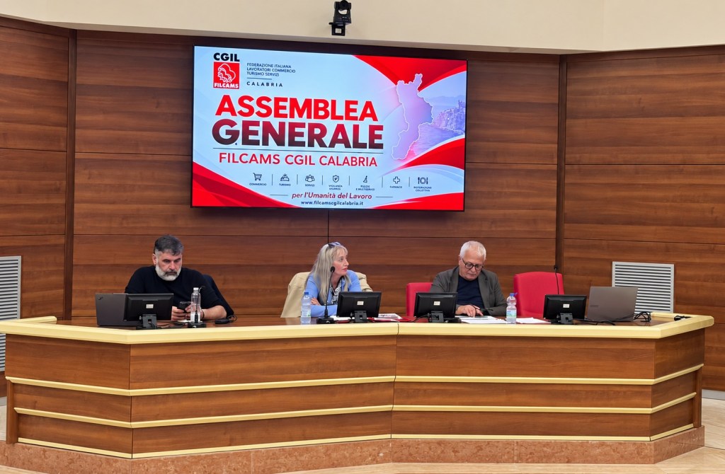 Tre relatori al tavolo della presidenza dell'assemblea generale FILCAMS CGIL Calabria, sotto lo schermo con il logo del sindacato