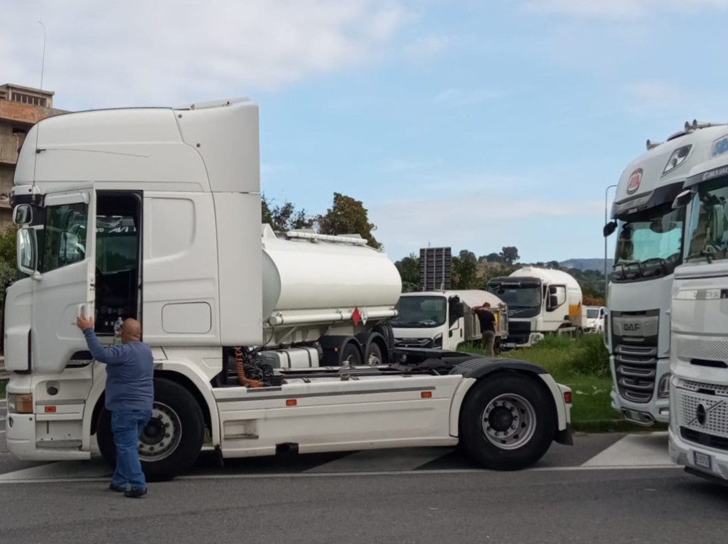 Un uomo accanto alla cabina di un camion cisterna bianco, con altri mezzi pesanti fermi sul piazzale