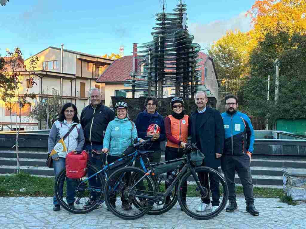 Sette persone in posa con due biciclette in una piazza davanti a una scultura ad albero a Gambarie d'Aspromonte