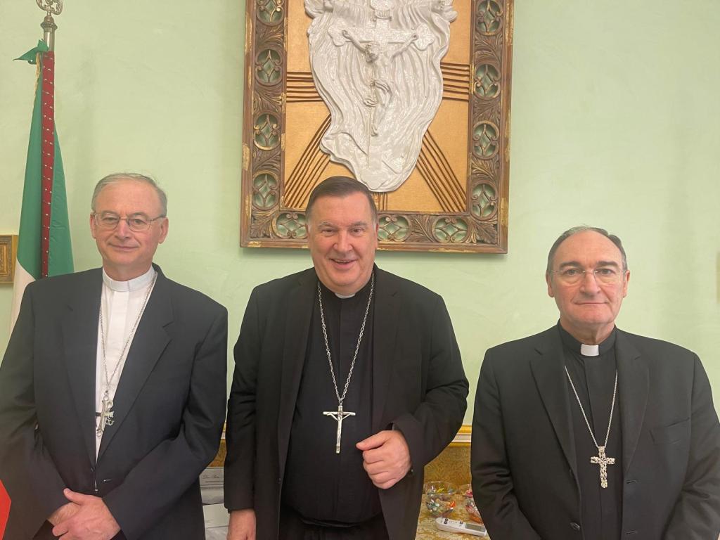 Tre vescovi in abito ecclesiastico posano davanti a una parete con un crocifisso, dopo il rinnovo della presidenza della Conferenza episcopale calabra