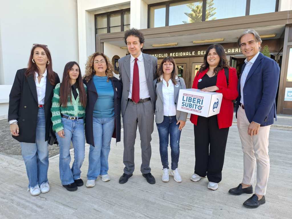 Un gruppo di persone in posa davanti all'ingresso del Consiglio regionale con una scatola della campagna Liberi Subito