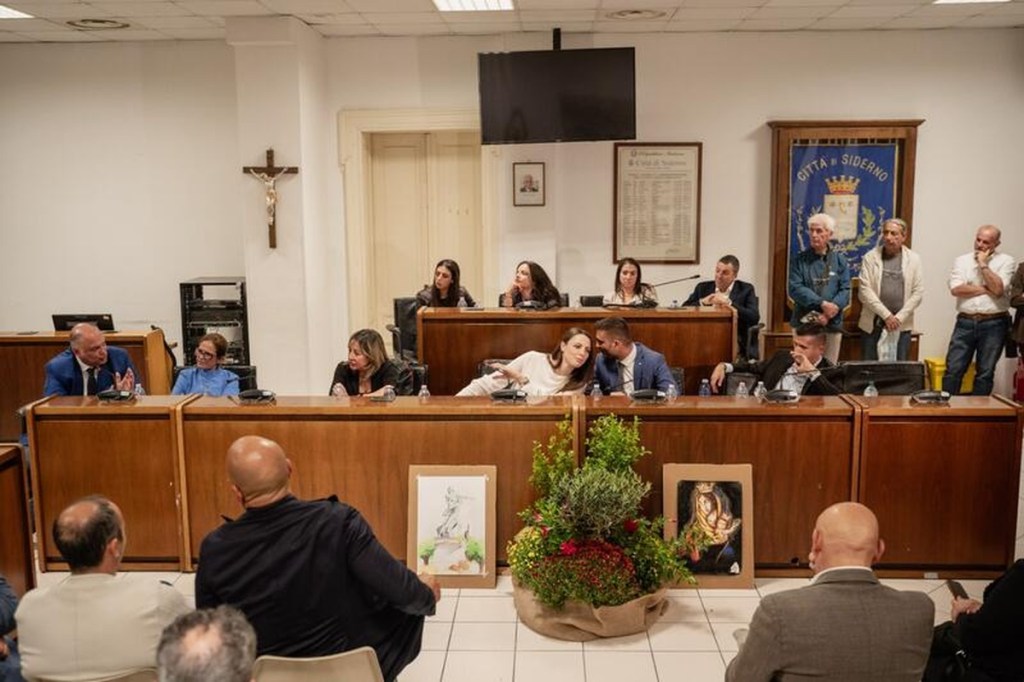 Relatori ai banchi di legno della Sala del Consiglio Comunale di Siderno con il pubblico in primo piano e il gonfalone alle spalle