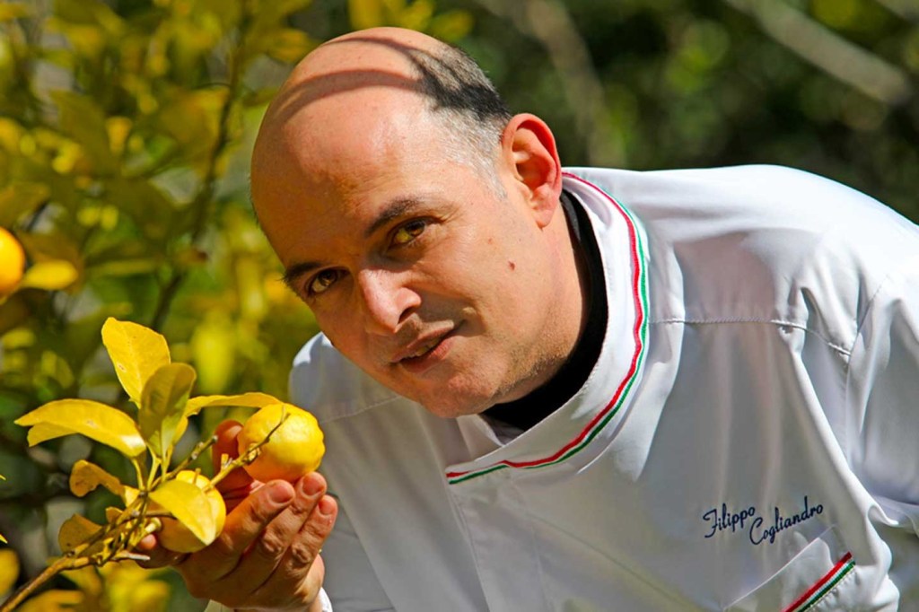 Lo chef Filippo Cogliandro in divisa bianca osserva un frutto giallo su un ramo di agrumi