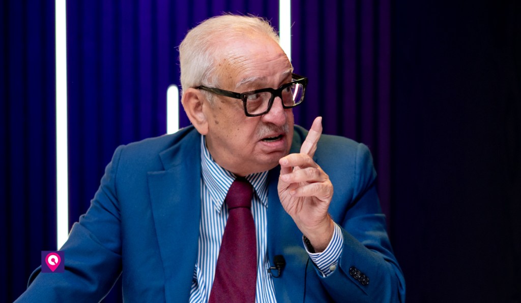 Gabriele Martino, con occhiali neri e giacca blu, parla in studio alzando l'indice