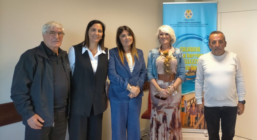 Cinque persone in posa davanti a un pannello dell'Assessorato regionale Inclusione sociale e welfare della Regione Calabria