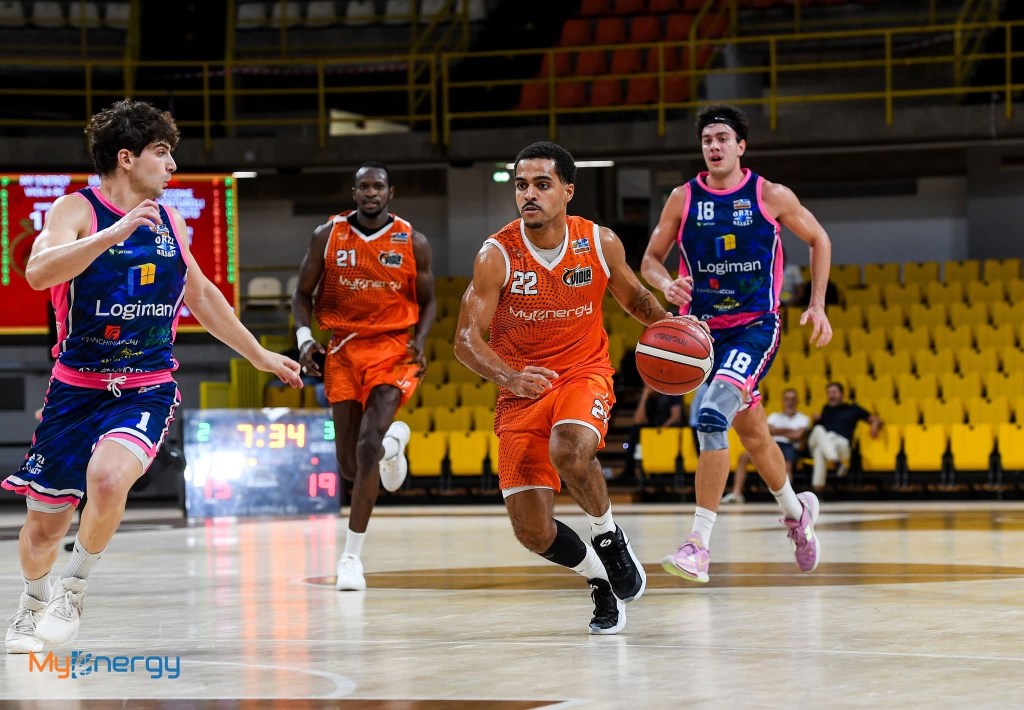 Giocatore in maglia arancione Myenergy con il numero 22 palleggia in campo davanti a due avversari in maglia blu