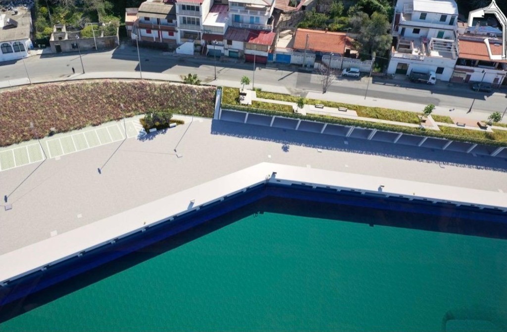 Rendering dall'alto di una banchina sul mare con area pedonale e fascia verde accanto alla strada e agli edifici