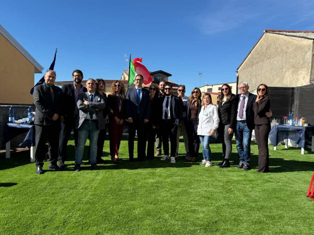 Gruppo di persone in posa su un prato sintetico, con la bandiera italiana e quella europea, durante l'apertura dei nuovi locali