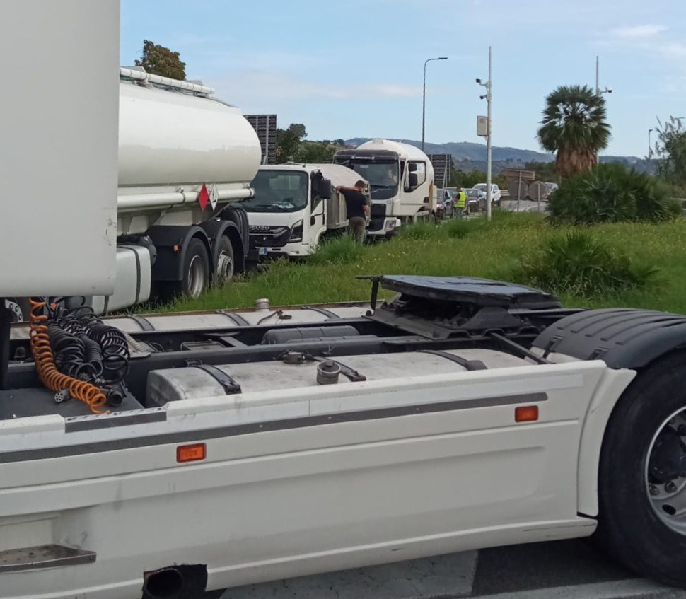 Autocisterne e camion fermi su un'aiuola dello svincolo, con alcuni conducenti accanto ai mezzi