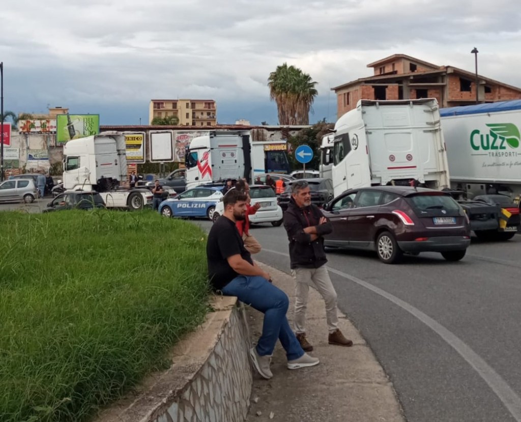 Due uomini sul bordo della strada davanti ai camion fermi, con una volante della Polizia sullo sfondo