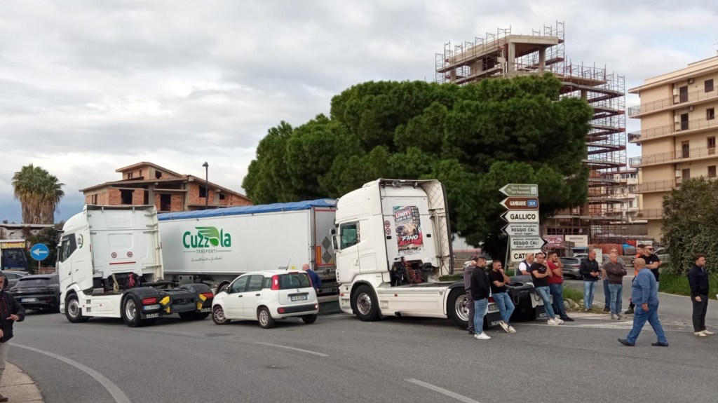 Camion fermi sulla rotatoria dello svincolo di Gallico, con un gruppo di autotrasportatori in piedi lungo la carreggiata