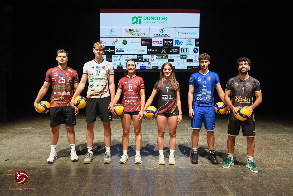 Sei atleti, uomini e donne, in maglie da gara diverse con un pallone in mano davanti a un maxischermo con i loghi degli sponsor