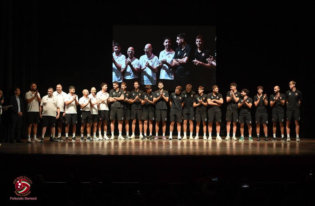 Giocatori e staff in maglia nera e bianca schierati in fila sul palco, con un maxischermo alle spalle