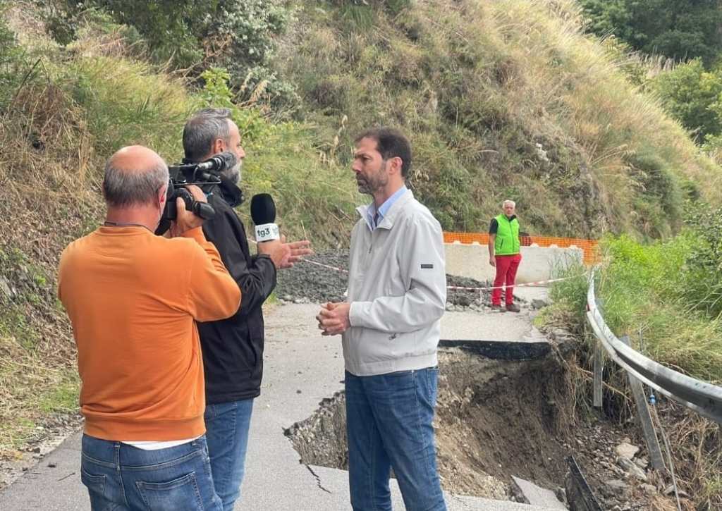 Giornalisti del Tg3 intervistano un uomo su una strada franata e transennata, con tecnici sullo sfondo