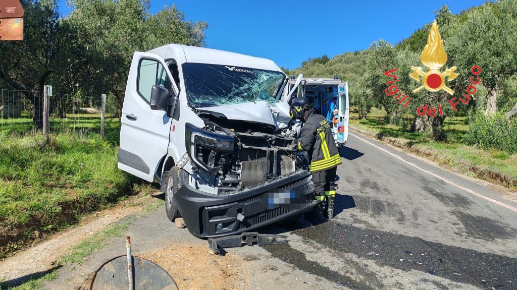 Un vigile del fuoco ispeziona il furgone con il frontale distrutto, con un'ambulanza dal portellone aperto sullo sfondo