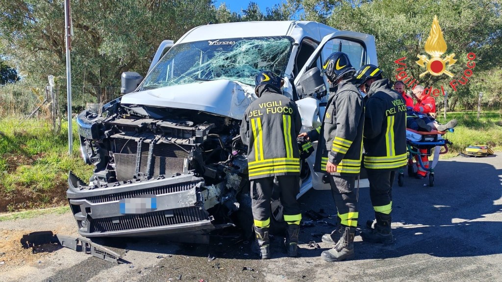 Tre vigili del fuoco davanti al furgone con il frontale distrutto, mentre una persona su una barella viene assistita dai soccorritori